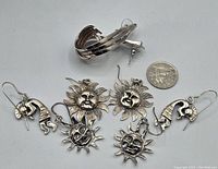 Four pairs of silver earrings displayed showing various styles including sun faces, Kokopelli figures, and twisted modernist hoops.