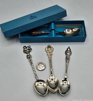 Four sterling silver souvenir spoons displayed with a quarter for size and blue Birks box containing one spoon.