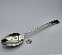 Full view of large sterling silver serving spoon with a quarter coin for size comparison, showing length and shape.