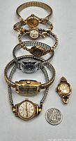 Seven vintage ladies' wristwatches arranged in a line with a 10-cent coin for size reference.