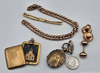 Photo of lot showing gold-tone curb chain bracelet, two lockets (one oval with floral interior and one rectangular with church image), and two pairs of cufflinks alongside a quarter for scale.