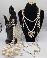 Full lot of four pearl necklaces displayed, showing variety in pearl sizes and styles including long strand and bow pendant necklace