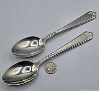 Two Birks sterling silver spoons placed next to a quarter for size comparison, showing entire spoons with polished finish.