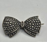 Close-up of the sterling silver bow brooch showing detailed dotted texture and shape.