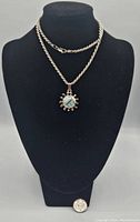 Full view of the pendant and chain displayed on a mannequin bust, showing the length and style of the necklace and the sunburst pendant with blue larimar stone.