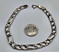 Full view of the bracelet laid flat next to a Canadian quarter for scale, showing chain design and length.