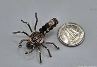 Front angled view of the sterling silver scorpion brooch placed next to a quarter for scale, showing detailed legs and pincers.