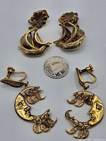 Top-down photo of two pairs of vintage damascene long drop earrings: one pair shaped like ships and another pair shaped like crescent moons, size reference with coin.
