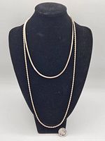 Two sterling silver chains displayed on a black bust, one chain longer and flat herringbone style, the other shorter twisted rope style, showing length and overall appearance.