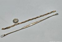 Two tri-colour sterling silver bracelets shown on a flat surface beside a coin for size reference