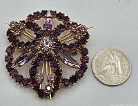Front view of the vintage purple rhinestone brooch with a quarter coin for size comparison.
