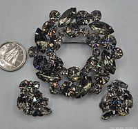 Front view of vintage grey rhinestone brooch with matching clip-on earrings, shows detailed rhinestone arrangement and approximate scale with coin