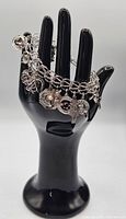 View of the vintage sterling silver charm bracelet displayed on a black mannequin hand showing the chain and hanging charms.
