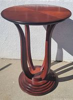 Side view of the wooden pedestal lamp table showing curved supports and stepped base.