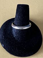 White gold band ring displayed on black velvet stand, showing smooth outer surface with star engravings.