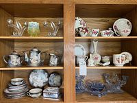 Overall shelving unit displaying all lot items including Dragonware pieces, floral cups, vases, and glassware