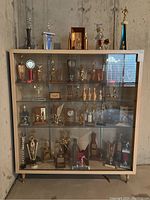 Front view of the 1950s wood and glass display cabinet containing trophies (not included). Shows overall form and glass shelving inside.