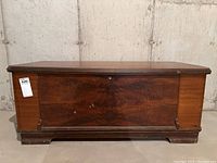 Front view of antique wooden blanket chest showing dark wood panel front and lighter wood sides with wear and marks.