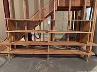 Four-piece homemade wooden stackable shelving unit assembled in basement, with natural unfinished wood surfaces, placed next to unfinished staircase and concrete floor.