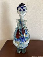 Front view of the Murano glass clown decanter showing the colorful spotted pattern, white clown face with blue details, black hat stopper, and clear glass accents.