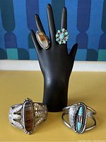 Display of two rings on black hand form with two cuffs in front on yellow surface, blue patterned background