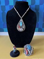 Necklace on black display bust with ring on stand and cuff beside