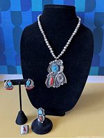 Overview of necklace, earrings, ring and pin on black display against patterned background