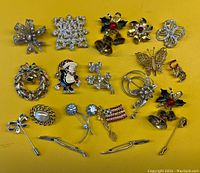Top-down view of all vintage brooches and pins laid out on yellow background showing a variety of designs including wreaths, bows, flags, and holiday themes.