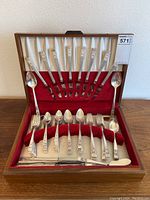 Full view of wooden flatware chest with red and ivory velvet lining, showing forks and spoons standing in slots, and knives and butter knife resting on bottom section.