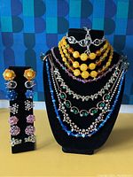 Front view of vintage costume jewelry including necklaces on display bust and clip-on earrings on stand