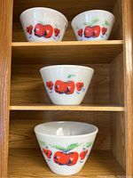 Stacked set of four Fire King mixing bowls on wooden shelf showing apples and cherries decoration.