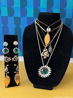 Full view of the vintage jewelry lot showing four layered necklaces on a bust and three pairs of clip-on earrings on a stand beside it.
