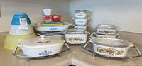 View of full collection of vintage Pyrex bowls and covered dishes featuring Cornflower and Spice of Life patterns, some on metal stands, including yellow mixing bowls.