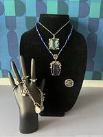 Overall display of two necklaces on black bust, charm bracelet and rings on hand stand