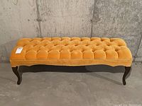 Front view of vintage velvet tufted bench showing mustard velvet upholstery and dark wooden legs with cabriole curves.
