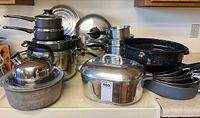 Photo of multiple vintage Wagnerware cookware pieces on countertop including roasting pans, pots, and stack of saucepans.