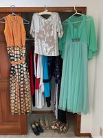 Full view of hanging dresses including gold and black patterned dress, silver sequin top, mint green chiffon dress, and shoes on floor.