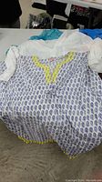 Top view of white bathing suit coverup with blue paisley print and yellow trimming on collar and hem