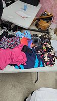 Multiple assorted women's bathing suits laid out on a table, featuring various colors and patterns including pink, black, floral, and animal print.