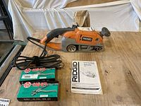 Ridgid large variable speed belt sander with dust bag, two new hand saw tooth sets, and instruction manual laid out on table.