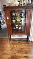 Full view of vintage mahogany wooden cabinet with glass front displaying various decorative items inside.