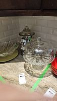 Glass cake plate with cover, glass punch bowl, cookie jar with cookie cutters, and green ceramic plate on counter