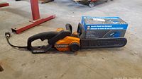 Full view of Worx electric chainsaw with its chain bar cover and PowerFist electric chain sharpener box next to it