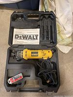 Open black plastic carry case containing yellow DeWalt cut-out tool with power cord, instruction manual, and sealed pack of extra bits.