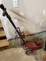 Full view of the red Torin Big Red 22 ton air/hydraulic floor jack with handle and wheels in a basement setting.