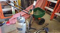 Full shot of all items including Premier Pro sprayer, green Scott seed spreader, metal weed puller, and sprinklers on floor near ladder.
