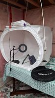 Front view of Neewer light box with the LED ring light inside, camera stand, backdrops and carry bag visible on table beneath the box