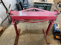 Front view of red metal bending brake on stand