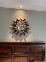 Front view of a sunflower themed metal framed mirror hanging on a light-colored wall above a wooden headboard.