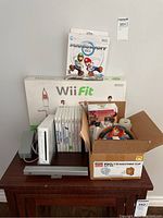 Full view of Nintendo Wii console setup including Wii Fit balance board box, Wii game cases, sensor bar, and box with controllers/accessories.